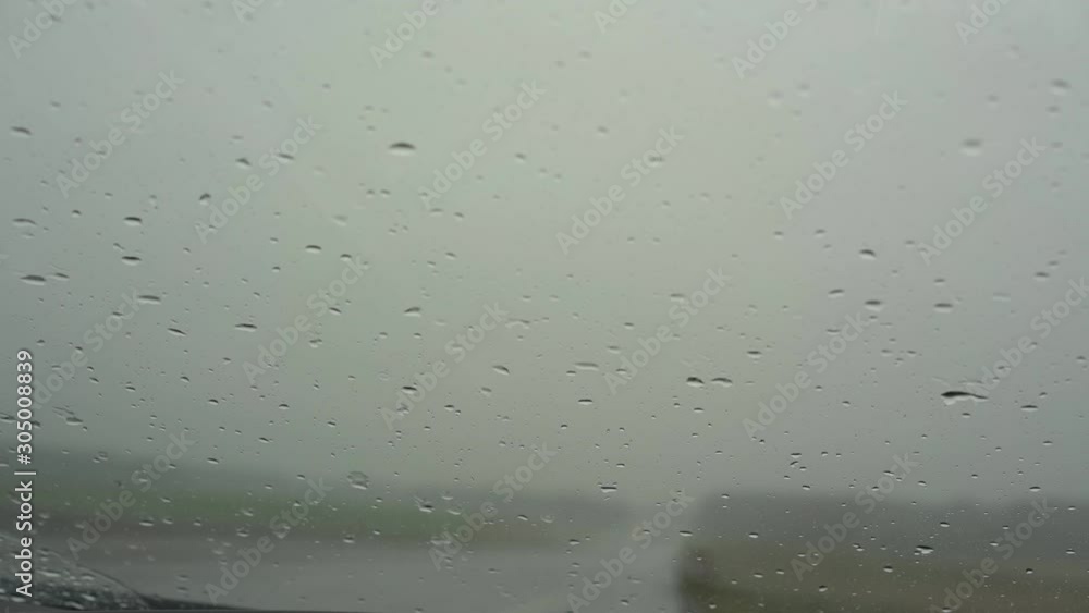 small rain drops fall on car windshield and black wipers move against driving truck silhouette in mist closeup small rain drops fall on car windshield and black wipers move against driving truck silhouette in mist closeup