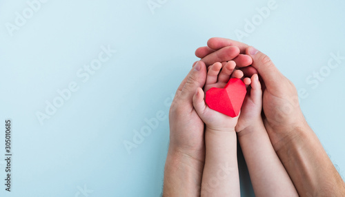 Cardiology and medical concept. Man and child hold red heart on light blue background. Top view, copy space