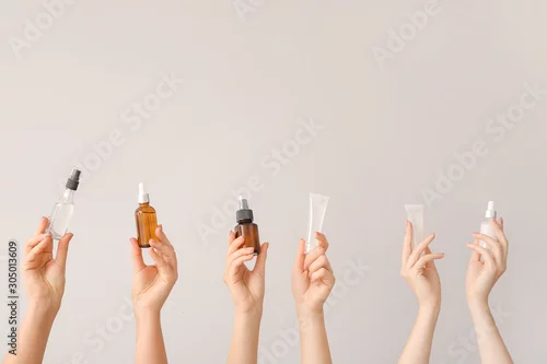 Obraz Female hands with different cosmetic products in bottles on grey background