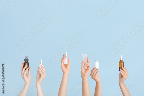 Female hands with different cosmetic products in bottles on color background