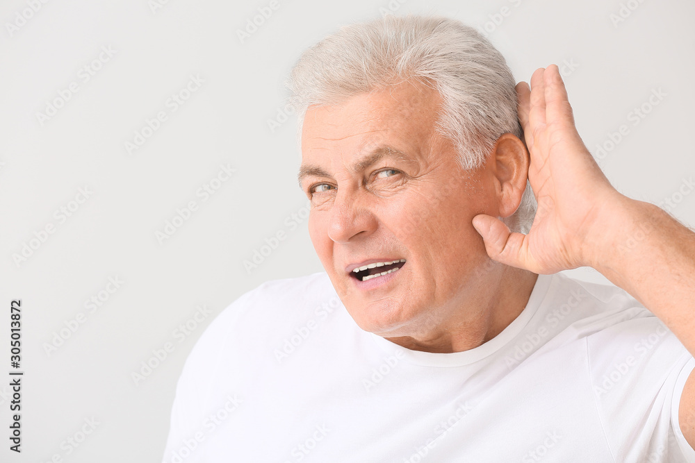 Mature man with hearing problem on light background Mature man with hearing problem on light background