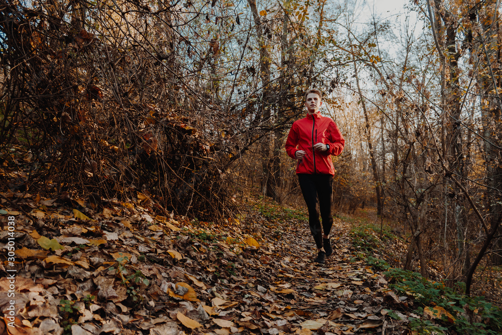 A guy in a red windbreaker runs in the autumn forest.