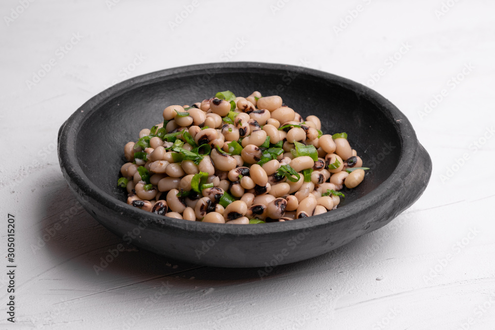 Cooked Fradinho beans in a black clay pot, isolated on a white background.