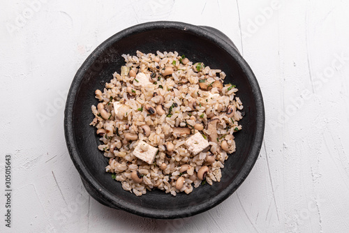 Baião de Dois - Brazilian Traditional Food - made with sausage, curd cheese, dried beef and rice in a black clay pot, on white background. Typical dish of Northeast Brazil.
