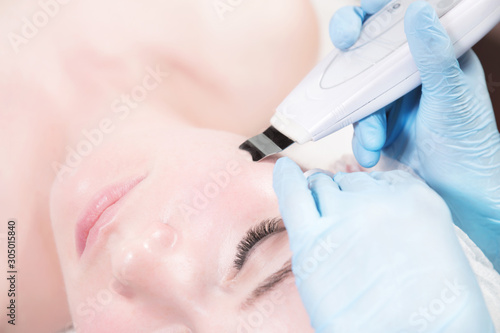 Close-up face of an attractive adult girl in a spa beauty salon at a reception by a professional cosmetologist for ultrasound cleaning of the face