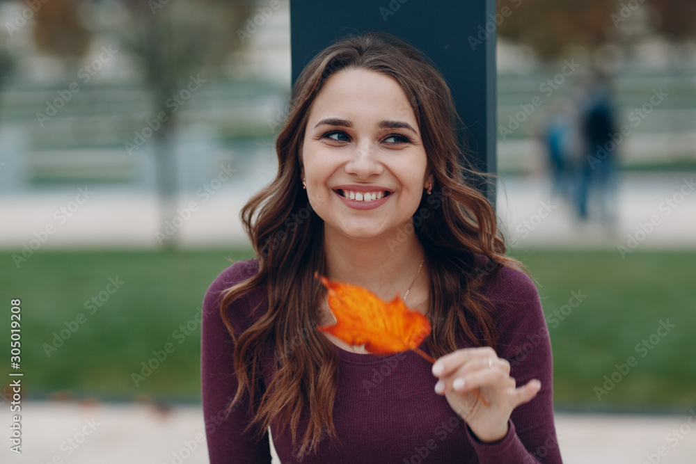 © primipil - Portrait of a young positive smiling woman with autumn yellow leaf