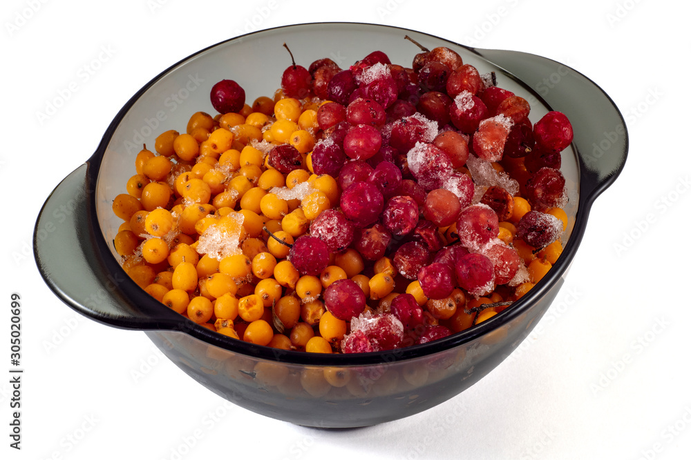 Frozen fruits of sea buckthorn and viburnum in a black transparent plate on a white background
