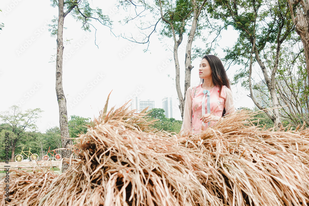 Portrait of Asian women in pink dress standing behind stacked straw Portrait of Asian women in pink dress standing behind stacked straw