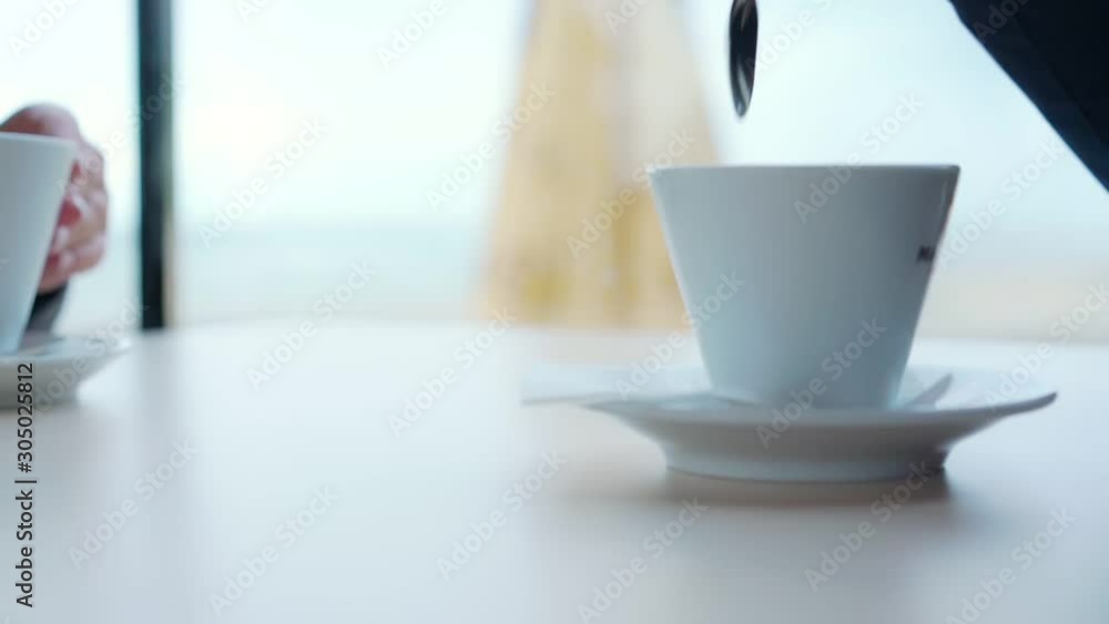 man stirs coffee in small white cup using metal spoon sitting at white table in restaurant closeup slow motion man stirs coffee in small white cup using metal spoon sitting at white table in restaurant closeup slow motion