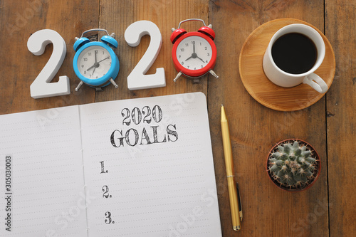 Business concept of top view 2020 goals list with notebook, cup of coffee over wooden desk