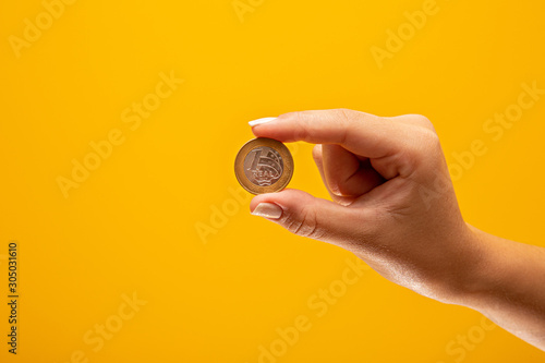 Hand holding one Real coin of Brazil on yellow background. Finance concept.