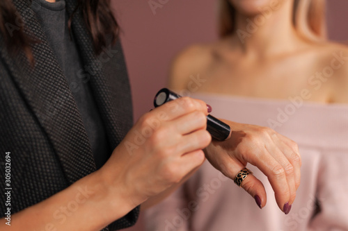 Woman makeup artist testing shades of bronzer swatch for face sculpting on her hand against blurred model on background, close up hands