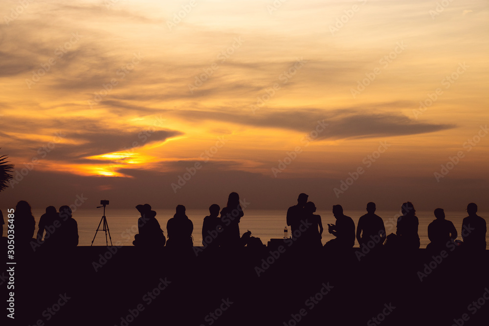 silhouette group of people sitting look at sunset light with orange sky at Phuket, Thailand