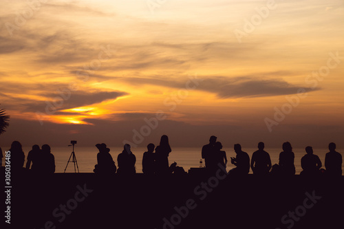 silhouette group of people sitting look at sunset light with orange sky at Phuket, Thailand