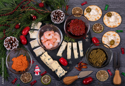 A dark cheese platter set with harissa and pesto pasta, parmesan cheese, gorgonzola, rosemary, olive and biscuits. Italian food with Christmas decor. Traditional breakfast or snack.