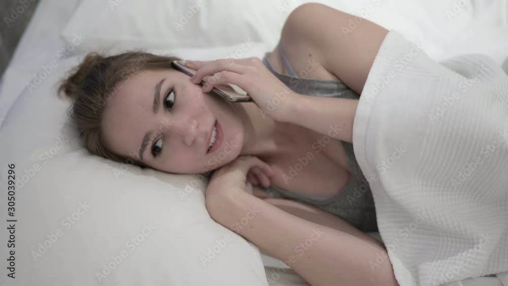 Cheerful Young Woman talking on Smartphone in Bed Cheerful Young Woman talking on Smartphone in Bed