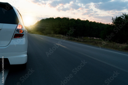 White car driving on the asphalt road with sunlight and forest in evening. 