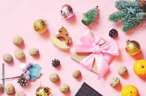 Flat lay winter aesthetics photo. Wrapped gift with pink bow ribbon, walnuts, fir tree branch, wooden horse, mandarins and golden balls. Christmas and New Year present and home decoration