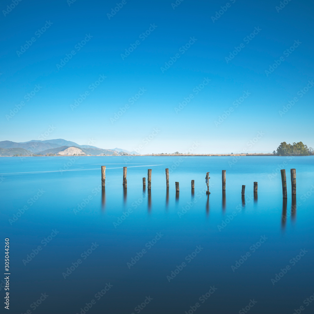 Wooden pier or jetty remains on a blue lake sunset and sky reflection on water. Versilia Tuscany, Italy