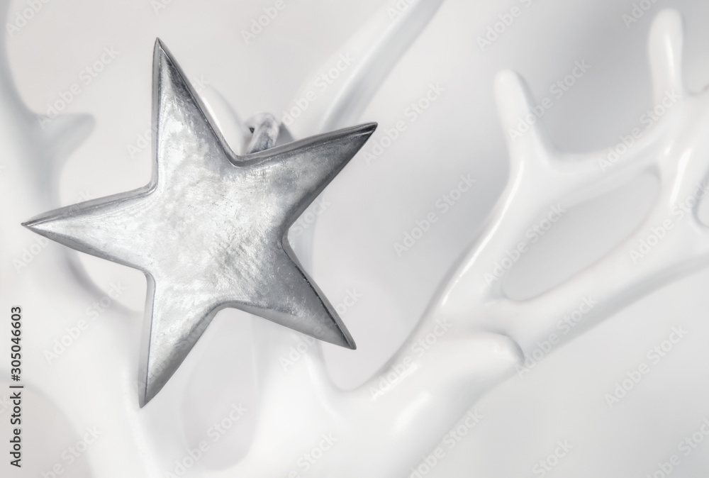 Obraz premium Single star on soft white background. Close up. The sterling silver star hangs on a porcelain tree or antler.
