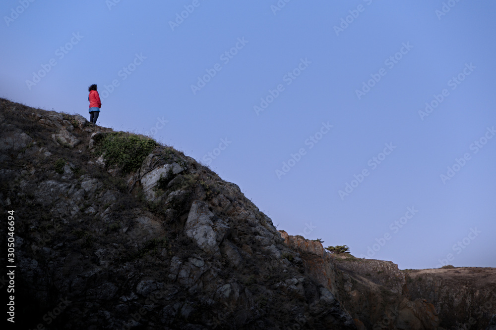 Woman looking at the horizon on top of cliff at blue hour