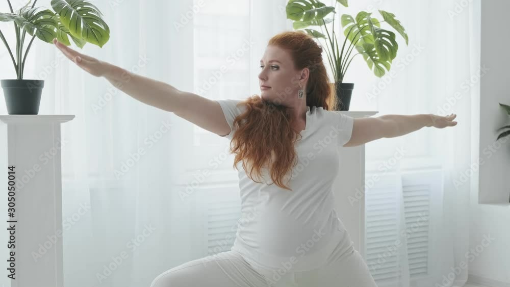 Young redhead pregnant woman doing stretching at home in slow motion. Pregnant doing yoga on floor at home. Medium shot in 4k, UHD Young redhead pregnant woman doing stretching at home in slow motion. Pregnant doing yoga on floor at home. Medium shot in 4k, UHD