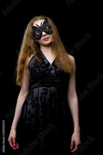 Beautiful little girl in theatrical mask. On a black background.