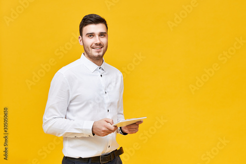 Modern technology and electronic devices concept. Studio shot of stylish positive young male manager using digital tablet for work. Businessman in formal wear holding touch pad portable computer