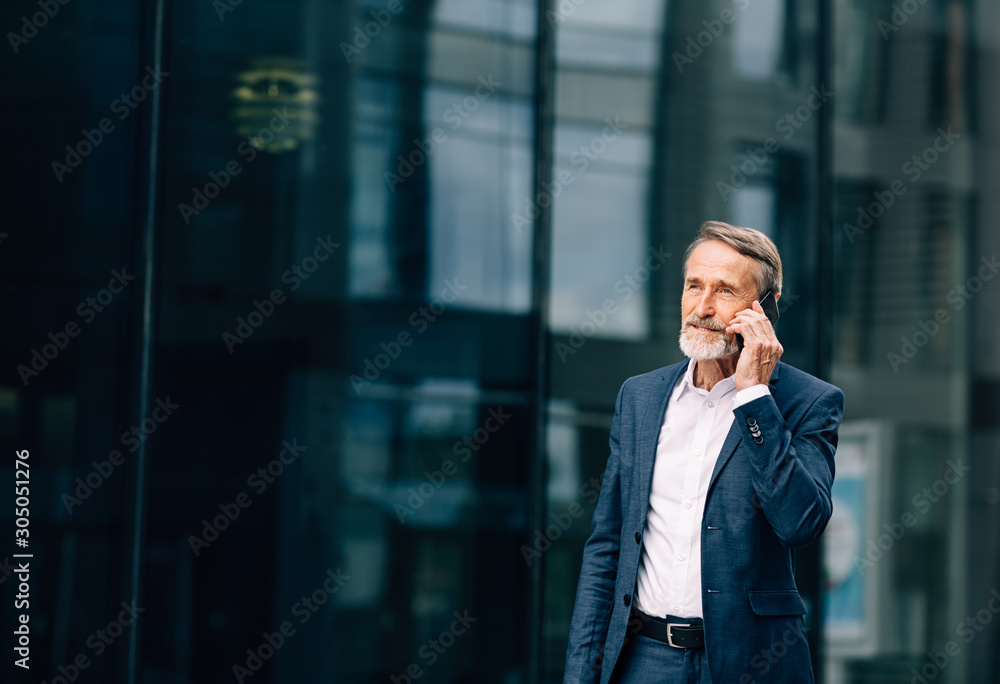 Senior businessman walking at office building and talking on cell phone Senior businessman walking at office building and talking on cell phone