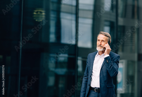 Senior businessman walking at office building and talking on cell phone