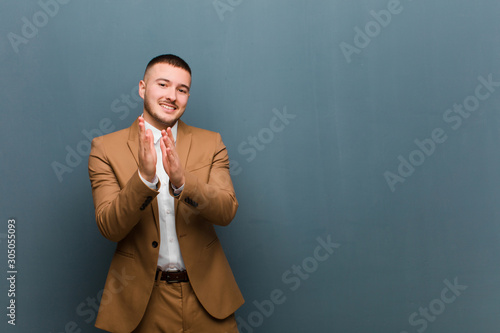 young handsome man feeling happy and successful, smiling and clapping hands, saying congratulations with an applause against flat background