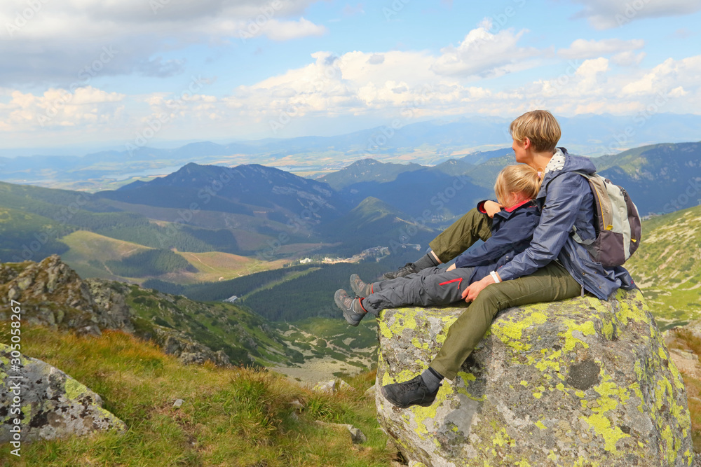 Mother and daughter sitting on large stone and watching mountain view