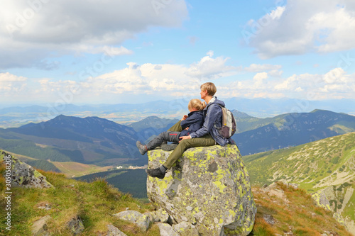 Mother and daughter sitting on large stone and watching mountain view © endostock