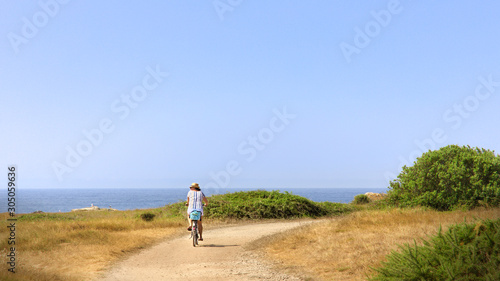 Woman riding bicycle along coastline © Aurelien