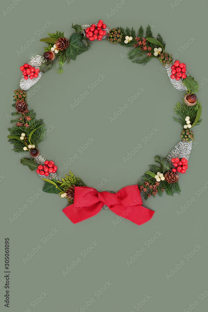 Natural Winter Christmas & New Year  wreath with snow covered fir, holly, ivy, mistletoe, pine cones, acorns & cedar leaves with red bow on green background with copy space.