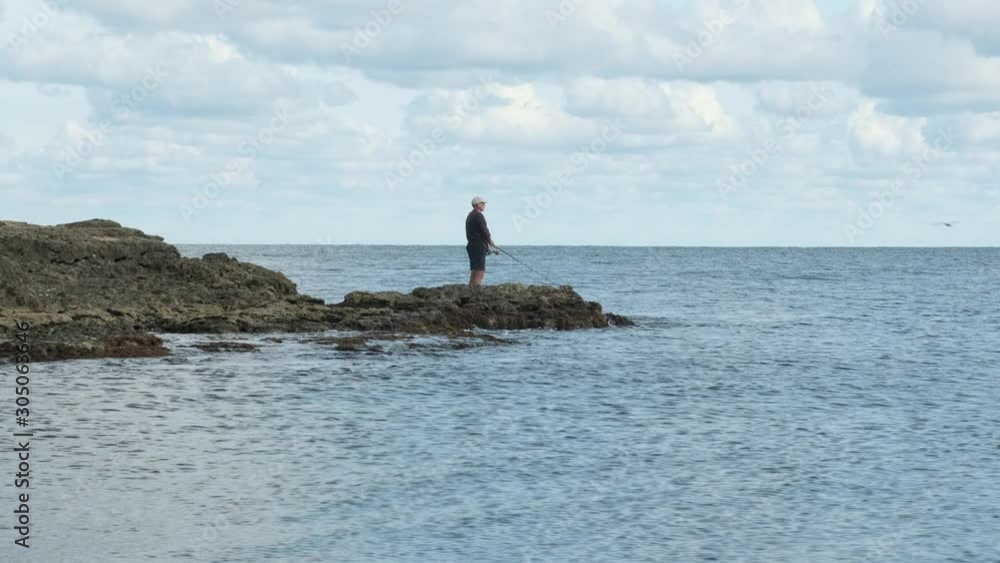 male fisherman is engaged in fishing standing on stones in sea. male fisherman is engaged in fishing standing on stones in sea.