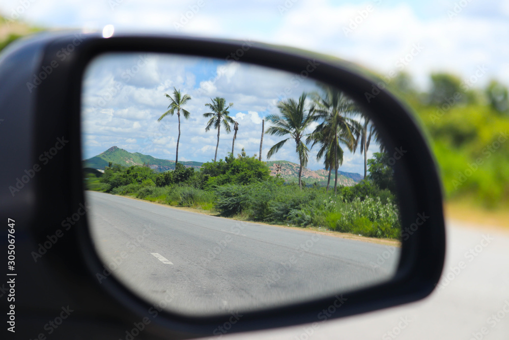 Natural Scenic Palm Trees Road and Blue Sky with Hills Mountains Clouds Seen Through The Car Side Mirror