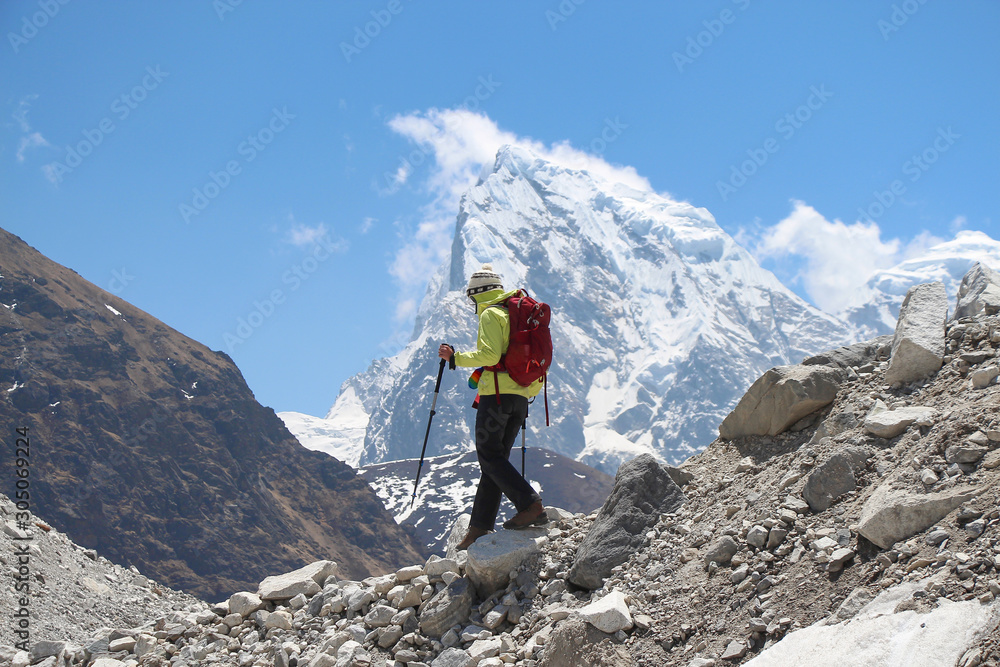 Hiker in yellow windbreaker walks on the slope of Ngozumpa glacier in Himalayas. Blurred Cholatse mountain peak is visible in the background. Route to Everest base camp through Gokyo lakes.