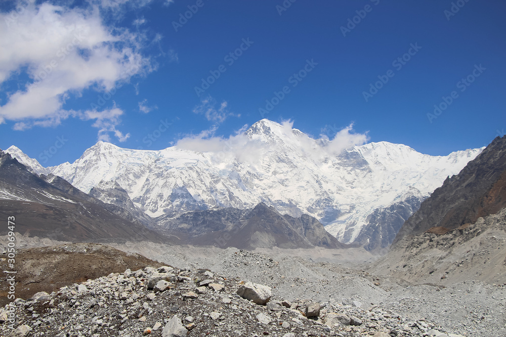 Snowy Cho Oyu mountain rises above Ngozumpa glacier covered with stones in Himalayas in Nepal. Route to Everest base camp through Gokyo lakes. Clear blue sky with some clouds.