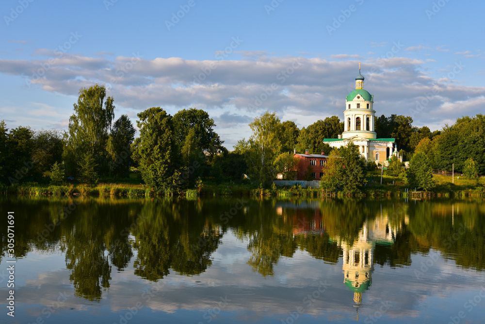 Beautiful landscape with lake, forest and the old chapel. Clouds in the blue sky.