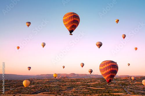 Top view to colorful hot air balloons flying over valleys and fields during sunrise. Turkey, Cappadocia.