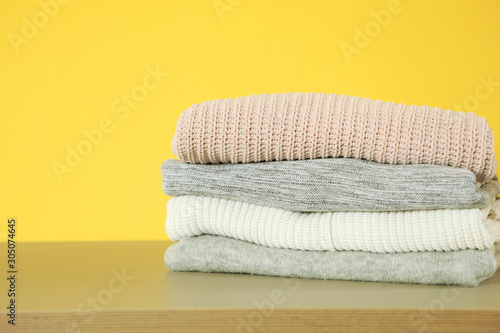 a stack of warm sweaters on the table on a colored background.