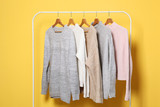 Warm sweaters on a wardrobe hanger on a colored background. Autumn, winter clothes.