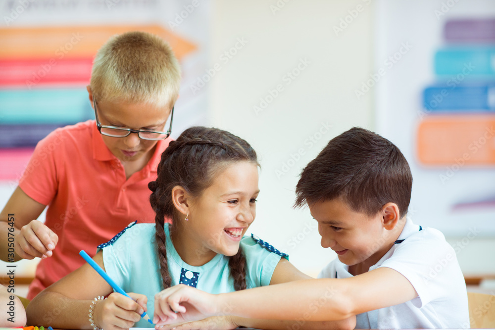 Happy elementary students sitting at desk and joyful discussing in classroom Happy elementary students sitting at desk and joyful discussing in classroom