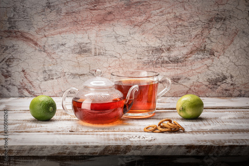 Still life on a light textured background glass teapot mug with poured tea limes on a table of whitish boards with a visible edge