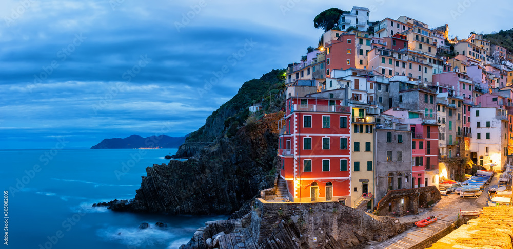 Evening panorama of the town of Riomaggiore in Cinque Terre National Park in November, multicolored small houses built on rocks turned on evening light of lanterns
