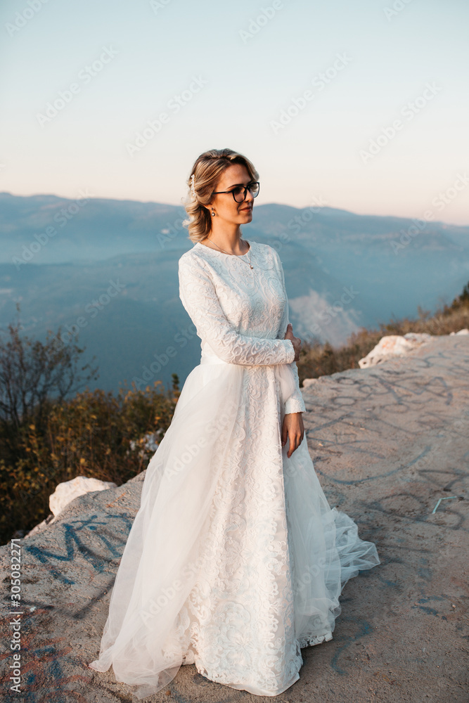 Beautiful elegant bride in lace wedding dress with long full skirt and long sleeves. Pretty girl in white. Nature, sunset time.