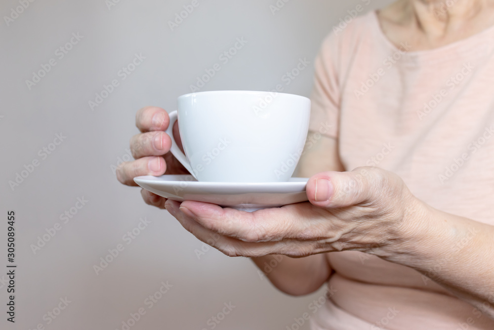 A senior woman holding a cup of coffee or tea in hands A senior woman holding a cup of coffee or tea in hands