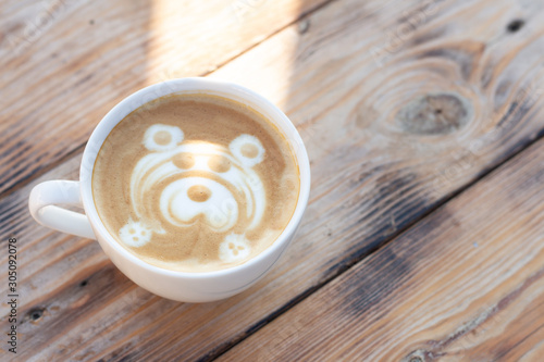 Cup of coffee on a wooden table. Cappuccino with a bear pattern and sunbeam.