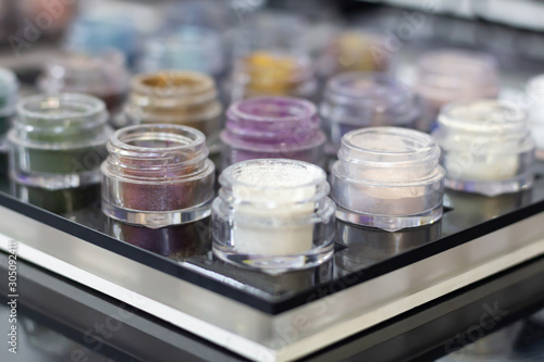 A lot of multi-colored eye shadows with glitter in jars on a black table. Close-up